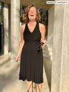Woman laughing in front of a building with her eyes closes wearing Miik's Zayd v-neck racerback dress in black holding her sunglasses 