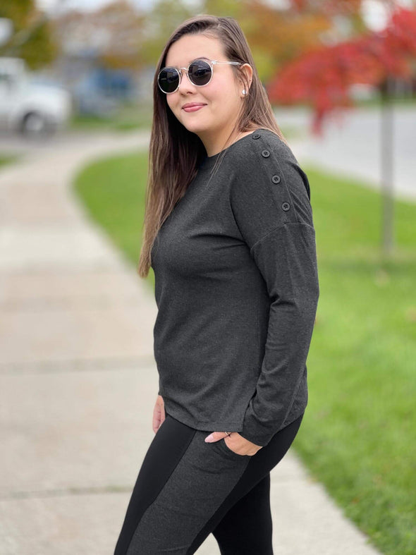 Woman standing on the sidewalk wearing Miik's Swansen drop shoulder buttoned top in grey with grey and black leggings.