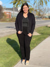Woman standing on a sidewalk wearing Miik's Emerson boxy blazer in black over a grey top with black pants.