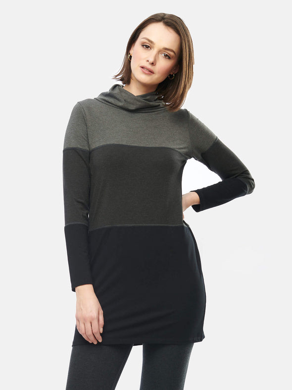 Woman standing in front of a wall wearing Miik's Hasha colourblock twisted cowl tunic in grey stripe and leggings.