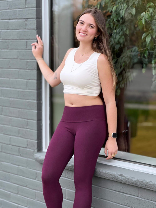 Woman smiling leaning against to a window wearing Miik's Lisa2 colourful high waisted legging in port melange with a white tank top