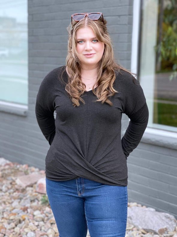 Woman standing in front of a building wearing Miik's Chenley twist-front top in grey with jeans.