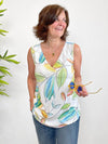 Woman standing in front of a white wall wearing Miik's Taz sleeveless inverted pleat top in tropical leaf print with jeans.