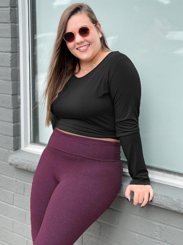Woman leaning against to a window smiling wearing Miik's Lisa2 colourful high waisted legging in port melange with a long sleeve cropped top in black