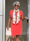 Woman opening the door smiling wearing a bright orange dress with Miik's Halona tie scarf in colourful leaf pattern tied around her neck.